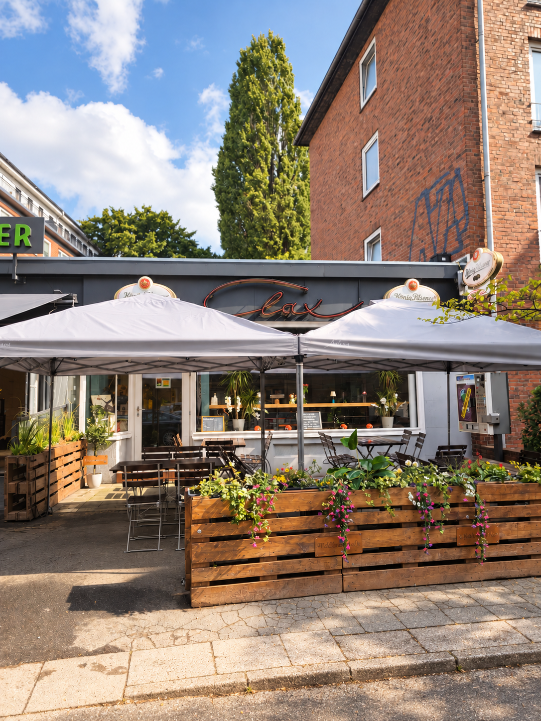 Clax-Terrasse am Tag mit Sonnenschirmen, Paletten-Beeten und Holztischen
